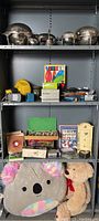 Full shelving unit view showing all miscellaneous items including stuffed animals, camera, chess set, and records along with silver plated items on top shelf