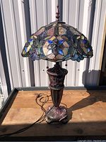 Full front view of Tiffany style table lamp showing stained glass shade and metal base with electrical cord.