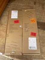 Two cardboard boxes containing Zenith Home bathroom tissue cabinets labeled with item number E9153WW, one box has handwritten notes indicating 'Bathroom Tissue Hideaway (White)'.