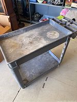 Right side angled view of gray plastic utility cart with visible spray paint marks and wear.