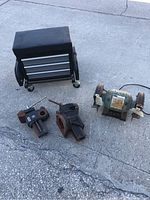 Photo showing two metal bench vices, a bench grinder, and a rolling tool cart seat with storage drawers on casters.