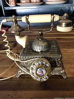 Front angled view of the vintage brass rotary telephone showing ornate detailing and coiled cord.
