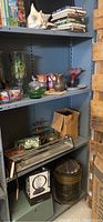 Shelving unit containing various decorative items including ceramic owls, glass bowls, a conch shell, cans, tins, boxes, and other miscellaneous household items.