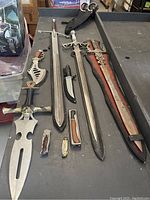 Overview of three swords and eight cutting utensils laid out on a surface