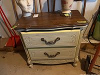 Front view showing painted cabinet with two drawers, metal hardware, wood top with curved edge, and some paint chips.