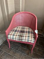 Front view of pink painted wooden chair with cane back and sides, removable plaid cushion on seat.