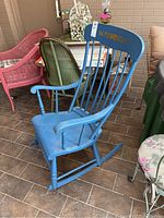 Blue wooden rocking chair angled view showing rocking legs, armrests, and floral painted backrest.