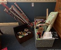 Multiple rolls of Christmas wrapping paper standing upright alongside a dark wood finished storage box containing various wrapping accessories.