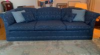 Front view of blue brocade upholstered couch with four cushions on a patterned rug in a cozy room.