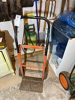 Front view of the orange and black metal moving dolly showing the flat base plate, handle, and wheels with worn paint.
