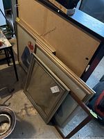 Four frames stacked against wall: two large matching framed textiles and two smaller empty frames; one frame missing backing.