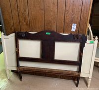 Both wooden headboards leaning against wood-paneled wall, showing dark wood headboard with carved details and panel inserts.