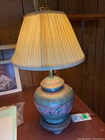 Full view of the oriental style lamp with pleated fabric shade lit, showing lamp height and design.