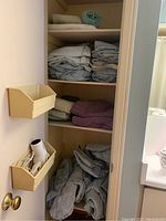 Photo of linen closet shelves containing folded towels and bedsheets in various colors and materials.