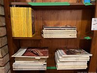 Wooden shelf with piles of loose vintage magazines including National Geographic and other varied titles, showing worn condition.