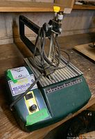 Overall front view of the green Brick mini scroll saw with power cord coiled on top, showing control knob and label on the side.