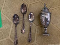 Full view of the 3 teaspoons and the decorative sterling silver salt shaker on a hexagonal tiled surface.