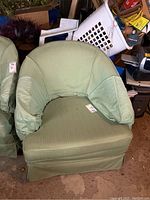 Front view of a green upholstered tub chair with slipcover in a cluttered space