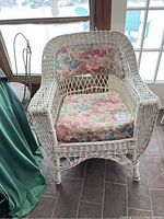 Front view of vintage white wicker chair with floral cushions showing the seat and backrest with cushion details and visible wear.