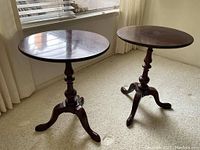 Two dark wood pedestal end tables shown with round tops, turned central pedestal, and tripod legs. Light surface scratches visible.