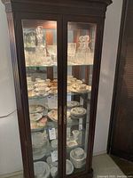 Front view of dark wood china cabinet filled with glassware and china to illustrate shelving and size