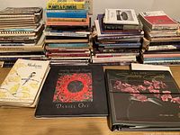 Wide view of multiple stacks of flower arranging books showing variety and quantity, including notable titles in foreground.