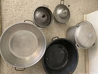 Top down view showing large hammered aluminum pot, medium black pot, metal soup tureen, smaller pot and large blue pot.