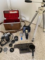 Overall view of complete camera equipment lot laid out, showing camera, lenses, flash, bag, tripod, and accessories on carpeted floor.