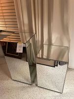 Two mirrored pedestals/end tables side by side, showing full reflective surfaces and relative height difference.