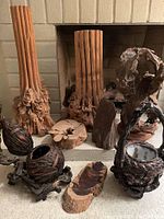 Wide view showing two tall carved bent wood pedestals, a driftwood loop, two dark slabs, two woven baskets, and a carved burl bowl on a hearth