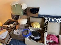 Overview of nine hats in original store boxes on couch