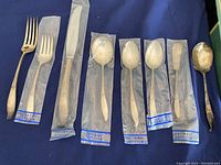 Eight pieces of Wallace sterling flatware displayed on blue background, some in plastic sleeves