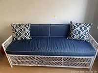 Front view of vintage white wicker sofa with dark blue cushions and two blue/white patterned pillows.