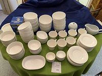 Full layout of assorted white dishes including cups, bowls in various sizes, plates, creamer, sugar bowl, and butter crock arranged on table.