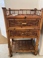 Front view of wicker side table showing top wicker surface, two drawers with wicker fronts and bamboo handles, bamboo frame.
