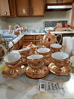 Photo showing the full coffee set on a kitchen counter, including coffee pot, cups with saucers, creamer, and sugar bowl, all gold-tone with red jeweled accents.