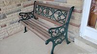 Front and side view of green cast iron garden bench with wooden seat slats placed on a stone porch corner.