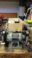 Front view of the Delta bench grinder sitting on a wooden surface, with a cardboard box behind it.