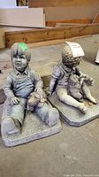Pair of heavy garden ornaments showing two seated children, one boy holding a dog.