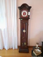 Full front view of grandfather clock showing wood carving, glass door, clock face and pendulum inside