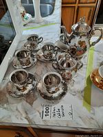 Full coffee service arranged on marble surface showing coffee pot, sugar bowl, creamer, four coffee cups and saucers with intricate gold and hand-painted romantic figure decoration.