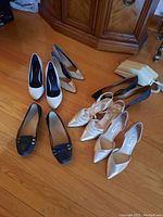 Eight pairs of ladies shoes arranged on hardwood floor showing variety of styles including high heels and ballerinas