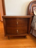 Front view of one of the Mid-Century Modern bedside tables showing two drawers and brass handles.