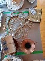 Photo of MCM metal drink holder filled with 7 glasses with gold trim and decorative gold design, boxed set of cheese forks and copper vases