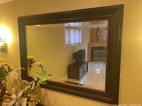 Photo showing the large wall mirror reflecting part of a room with furniture including TV stand and fireplace.