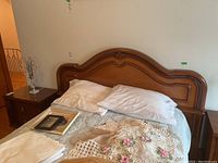 Queen size wooden headboard with bedding and pillows arranged on bed, bedside table with lamp on left side.