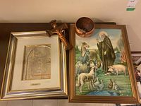 Photo showing two framed religious artworks, bronze crucifix, and copper bowl arranged on a surface.
