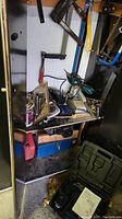 Shelf with various hand and power tools, cords, clamps, and cans under shelf including toolbox and Jerry can.