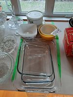 Top view of various bowls and glass bake dishes arranged on a table by a window, showing size and design