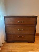 Front view of vintage wood dresser showing three drawers with metal handles and wood finish.